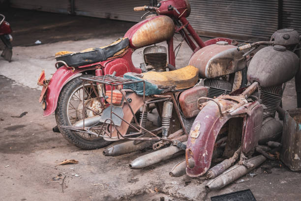 Old rusty motorcycle vehicle waste in waste scrap field with pile of old rusty metal wheels.